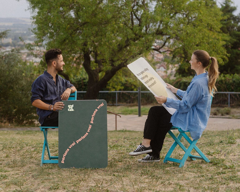 Deux personnes discutent sous les arbres d’un parc, avec de grandes cartes Quality Time